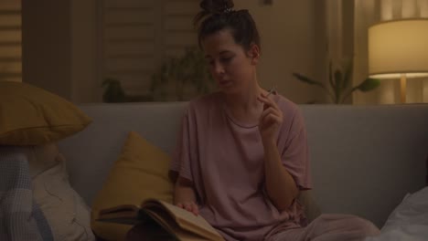 mujer leyendo un libro y fumando por la noche en el sofá