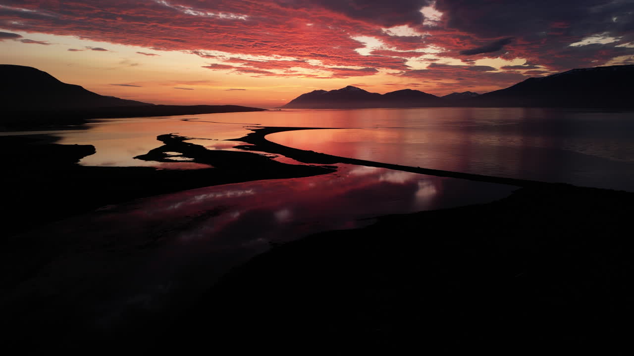 Panoramica aerea in allontanamento su luce arancione rossastra incandescente sui fiordi di Akureyri, Islanda