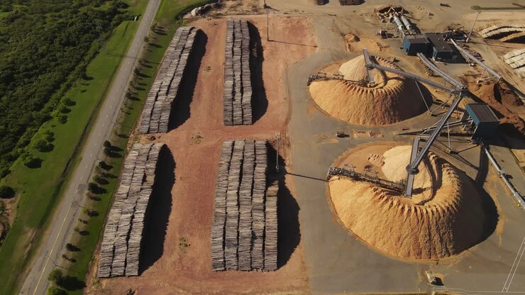 Aerial view showing heap of sawdust and stacked piles of trunks in paper mill factory
