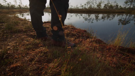 person in hiking boots standing by a calm swamp