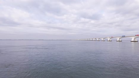 Vista-De-Pájaro-A-Baja-Altura-Sobre-El-Agua-Del-Oosterschelde-Junto-Al-Enorme-Puente-De-Zelanda-En-Los-Países-Bajos