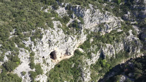 Montaña-De-Piedra-Caliza-Cubierta-De-Vegetación-Con-Una-Cueva-Natural-Toma-Aérea-Francia