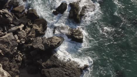 Drone-view-down-steep-cliff-of-waves-breaking-on-Canary-island-coastal-boulders