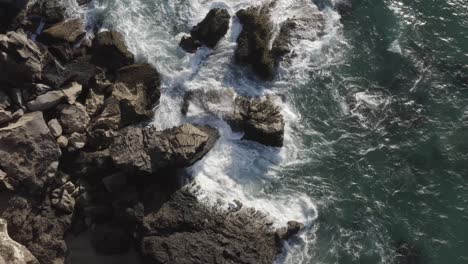 drone view down steep cliff of waves breaking on canary island coastal boulders