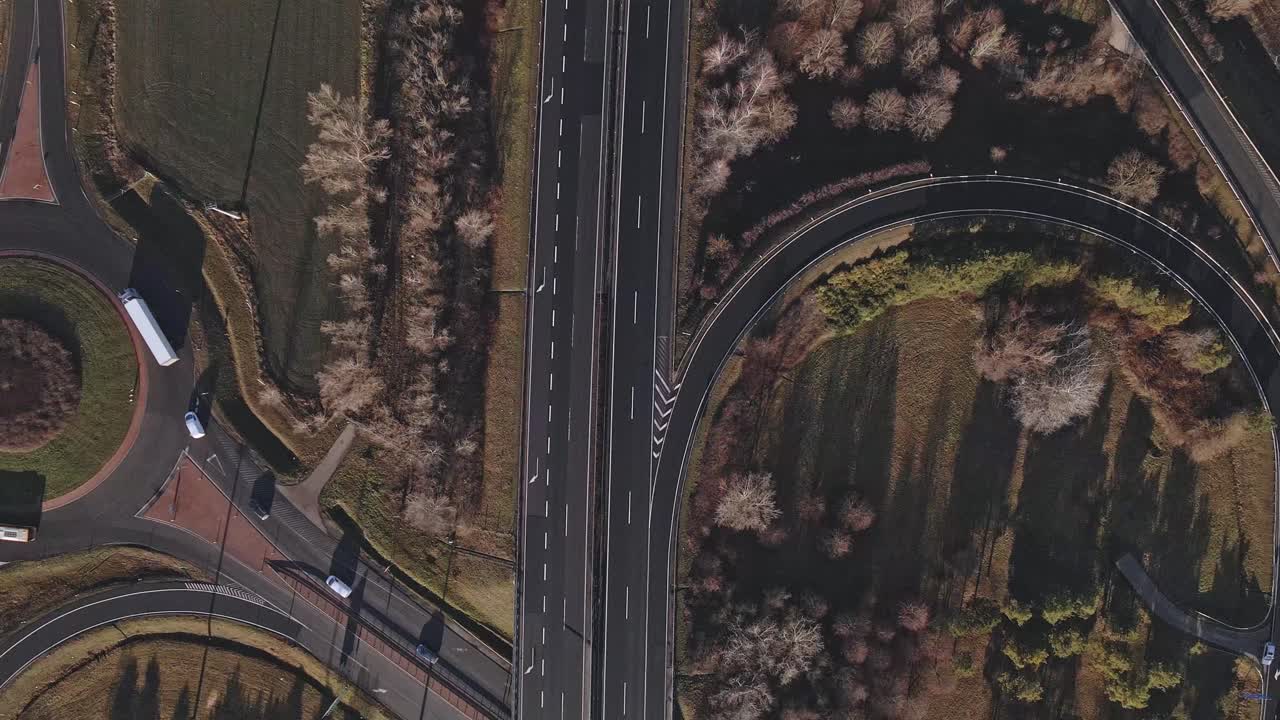A drone rises above the highway while cars and trucks travel on the road and the adjacent roundabouts.