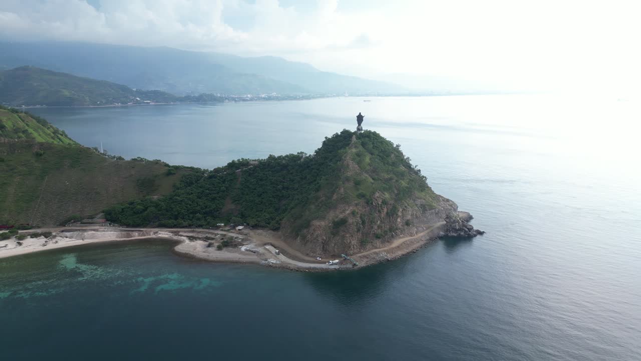 Aerial view of a large Jesus Christ statue on a hilltop overlooking the ocean and greenery.