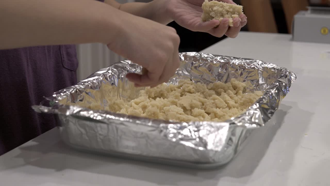 una niña prepara la corteza en una bandeja para hornear para hacer galletas de mantequilla millonarias