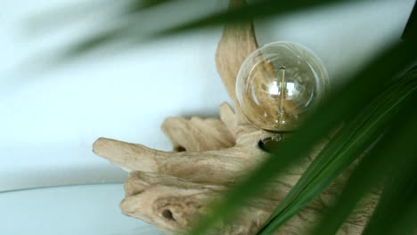 Hand-crafted-light-bulb-in-reclaimed-wood-seen-through-palm-leaves-in-a-modern-apartment-in-Santa-Monica-Los-Angeles-California