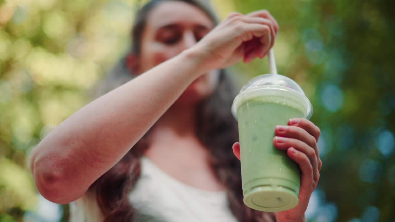 Close up of woman's hand holding an iced matcha latte outdoors