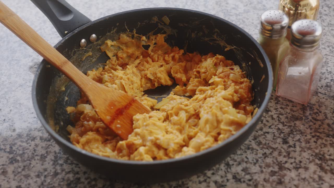 Black frying pan resting on marble with fresh scrambled eggs inside