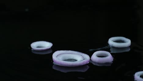 sliced onion rings falling on wet black surface and scatter around