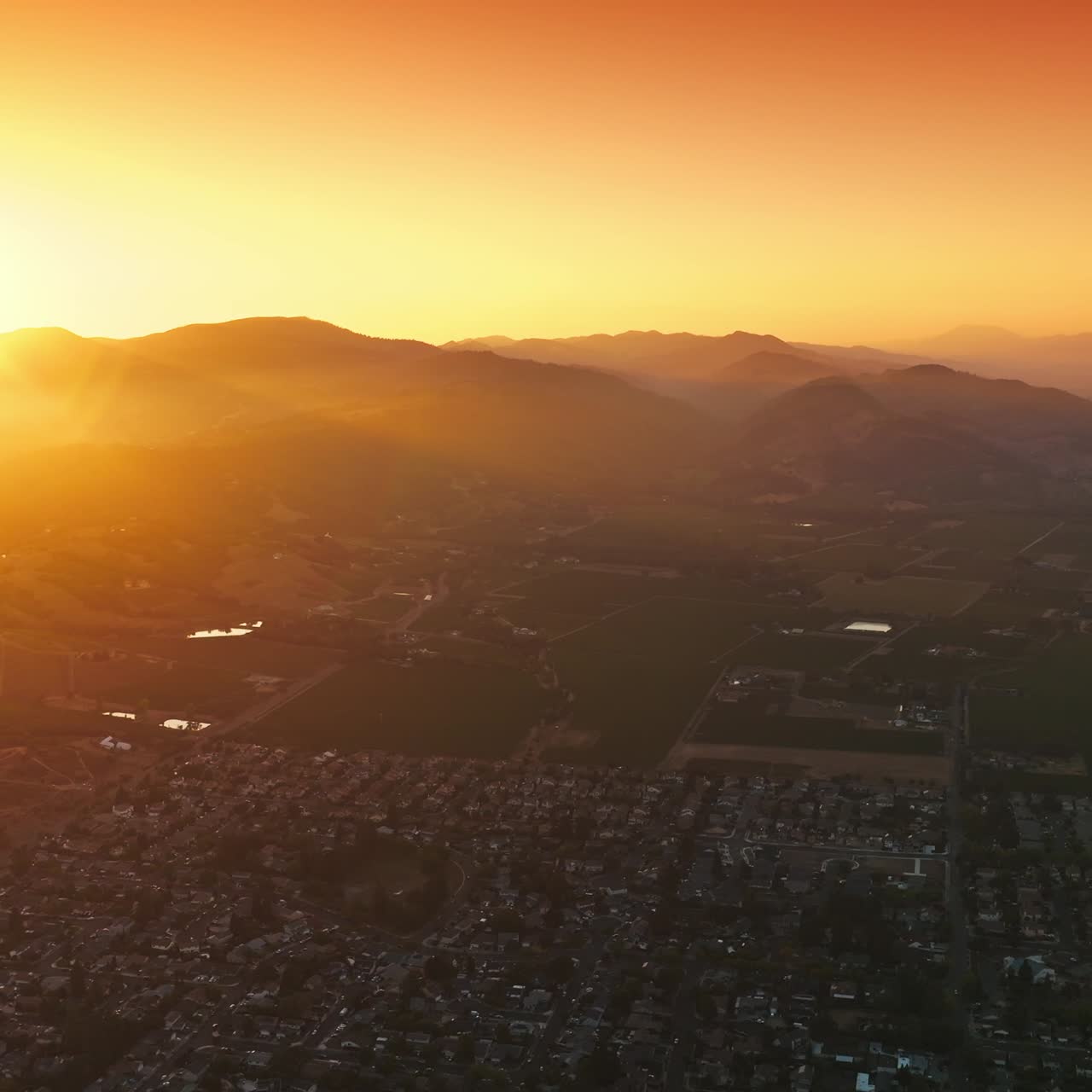 City with densely built architecture of low houses at sunset. Bright sun hiding behind the mountains. Aerial perspective