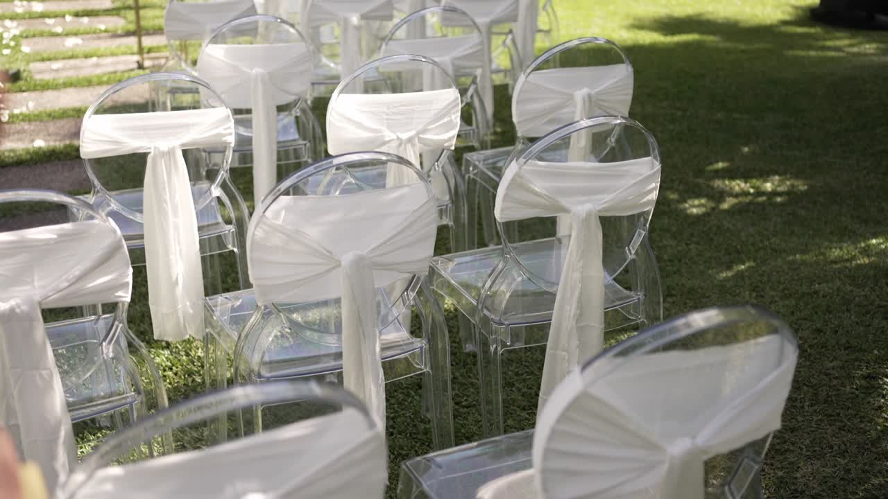 Sedie trasparenti con fasce bianche disposte per una cerimonia di matrimonio all'aperto su un prato erboso