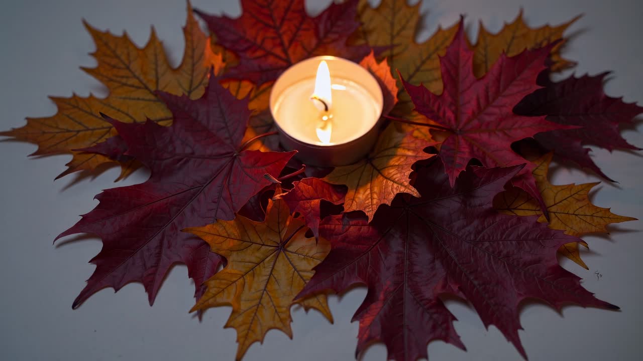 Top-down video shot of a lit candle surrounded by autumn leaves, creating a cozy, warm atmosphere