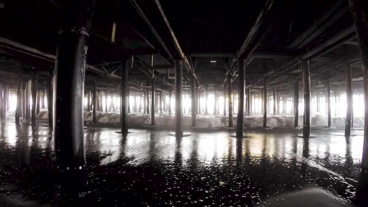 Waves lapping in and out under wooden pier on sunny day, California
