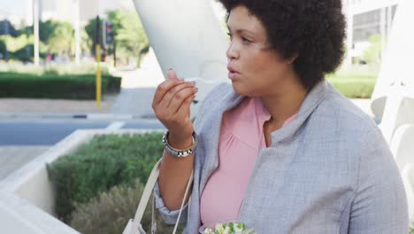 Plus-size-biracial-woman-eating-salad-in-city