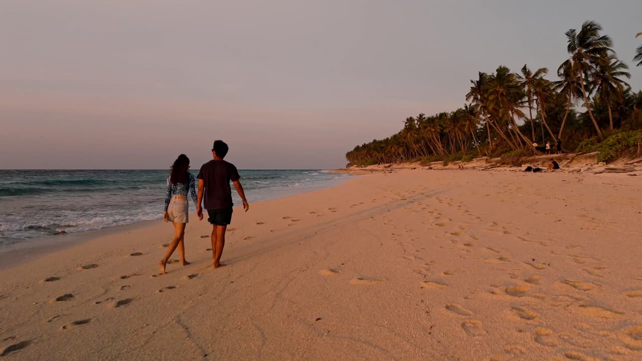 Romantic aerial drone view of a couple enjoying the golden sunset on Geiymiskih Fannu Beach in Fuvahmulah, Maldives.