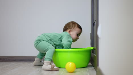 baby playing with a green basin and ball