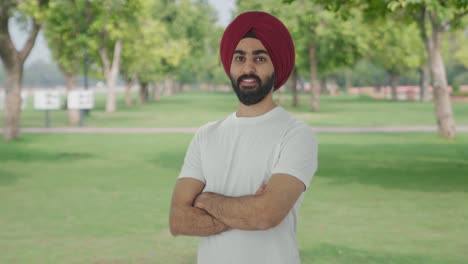 portrait of happy sikh indian man standing crossed hands in park