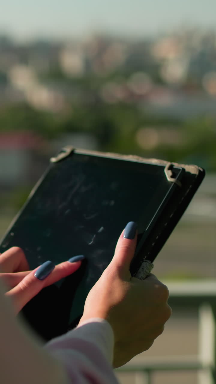 primer plano de manos operando tableta al aire libre con fondo borroso con edificios y objetos en movimiento, enfatizando la interacción con la tecnología en un entorno urbano bajo la luz del día brillante