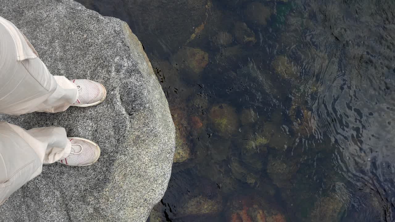 Vista dall'alto di piedi che poggiano su una roccia vicino all'acqua limpida di un fiume