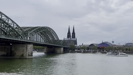 Kölner-Dom-Mit-Holzholandbrücke-Und-Rhein-Im-Vordergrund-Mit-Hauptbahnhof-Am-Fluss-Bei-Gutem-Wetter