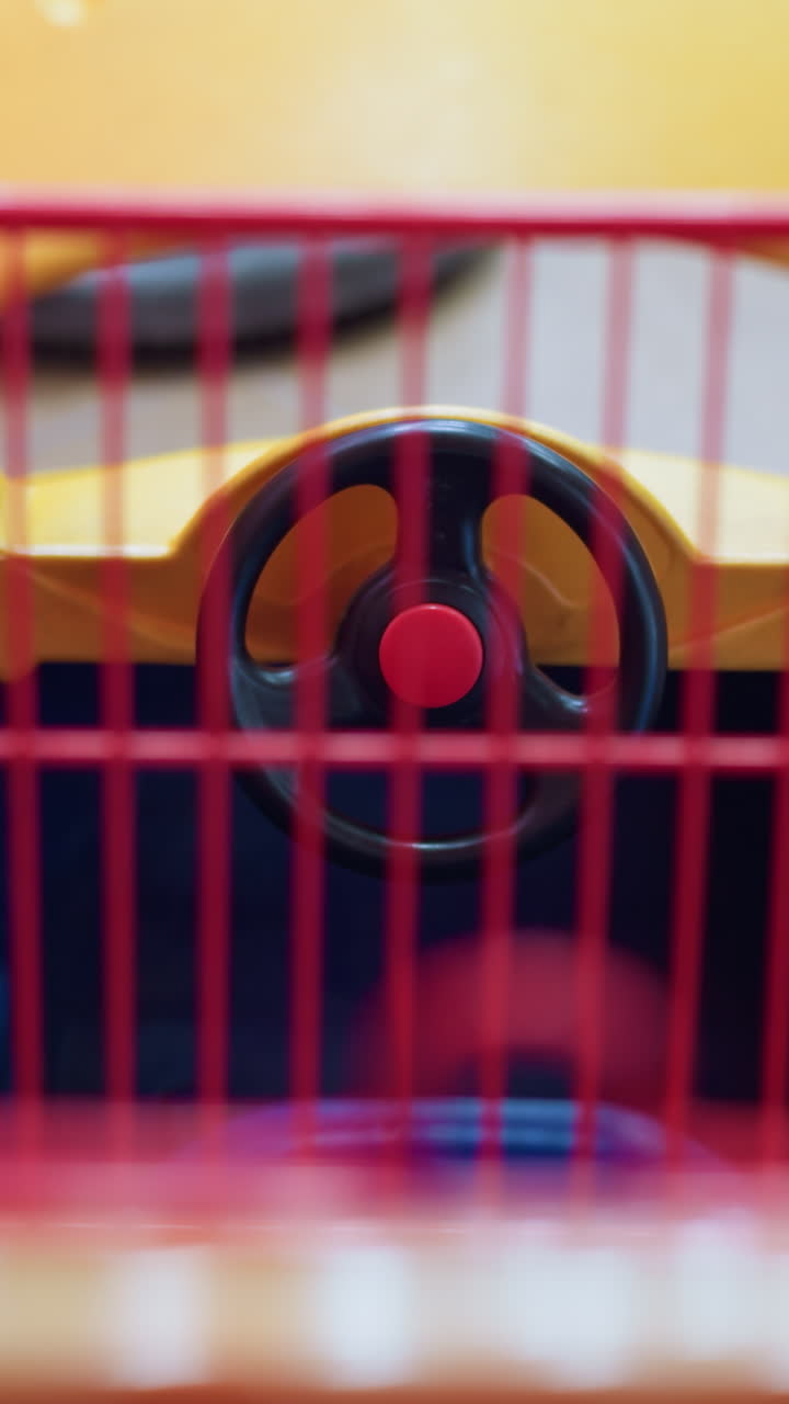 A close-up view of the interior of a children's shopping cart designed like a car, featuring a steering wheel and vibrant colors