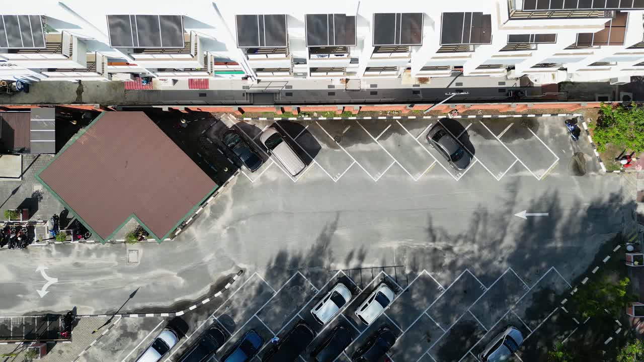Overhead shot of a parking lot in langkawi, malaysia, showcasing parked cars and marked spaces, with shadows indicating sunny weather and a nearby building adding urban context to the scene