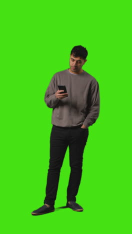 video vertical de larga duración de un hombre mirando un mensaje de texto en un teléfono móvil de pie contra la pantalla verde 2