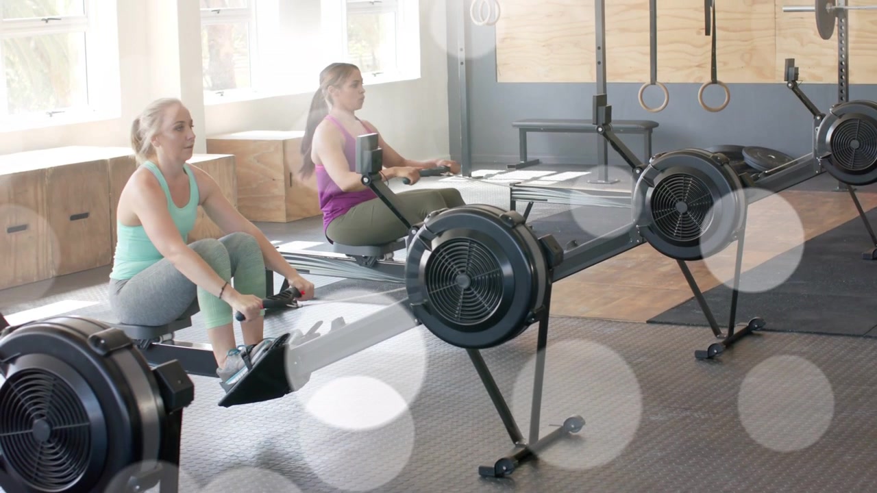 Camera focusing on right rower, two rowers rowing and syncing for fitness, bokeh overlaying