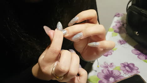 brunette woman is looking on her fresh made sparkling nails after her manicure