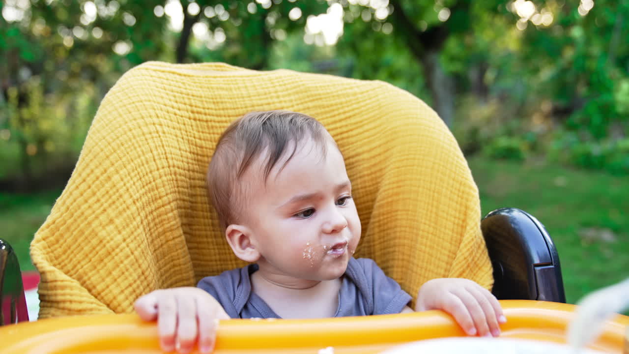 Feeding nice adorable child sitting in the yellow feeding chair. Caring mother feeding her baby from spoon. Close up. Blurred backdrop.
