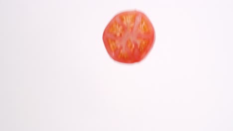 fresh red tomato slices raining down in slow motion on white backdrop in slow motion