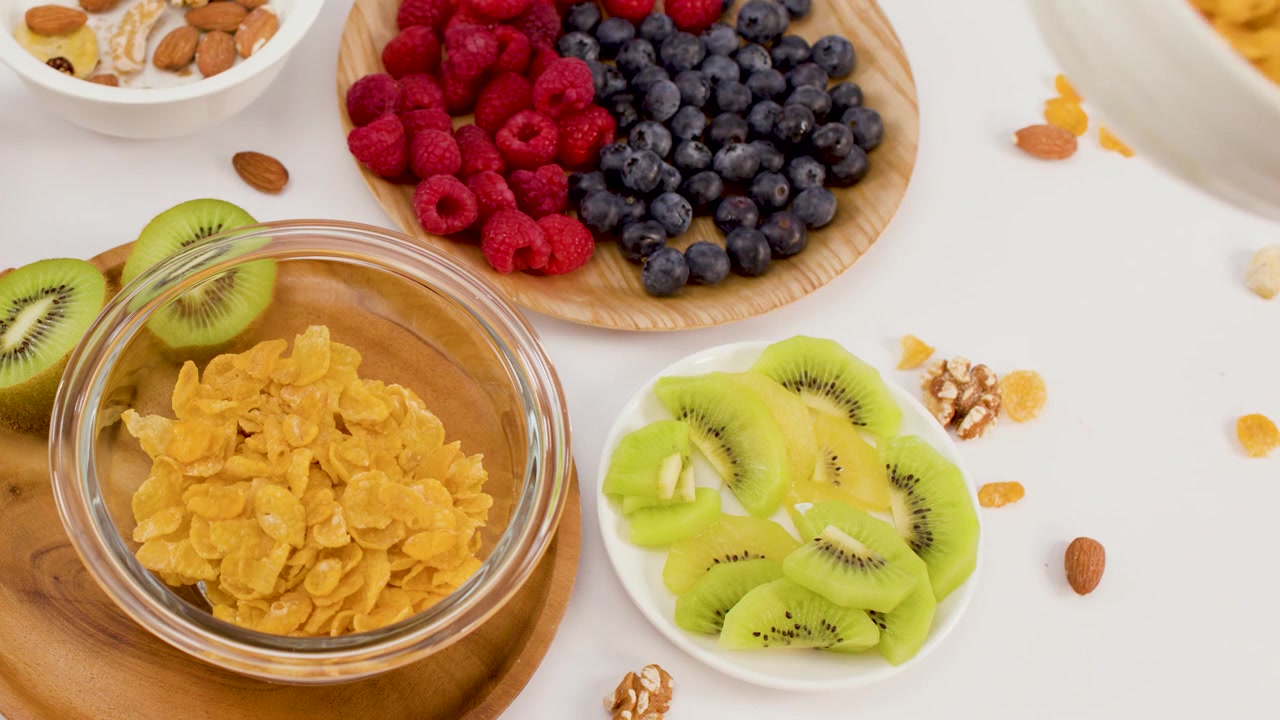 Mano che versa cereali in una ciotola circondata da kiwi, frutti di bosco e noci su sfondo bianco