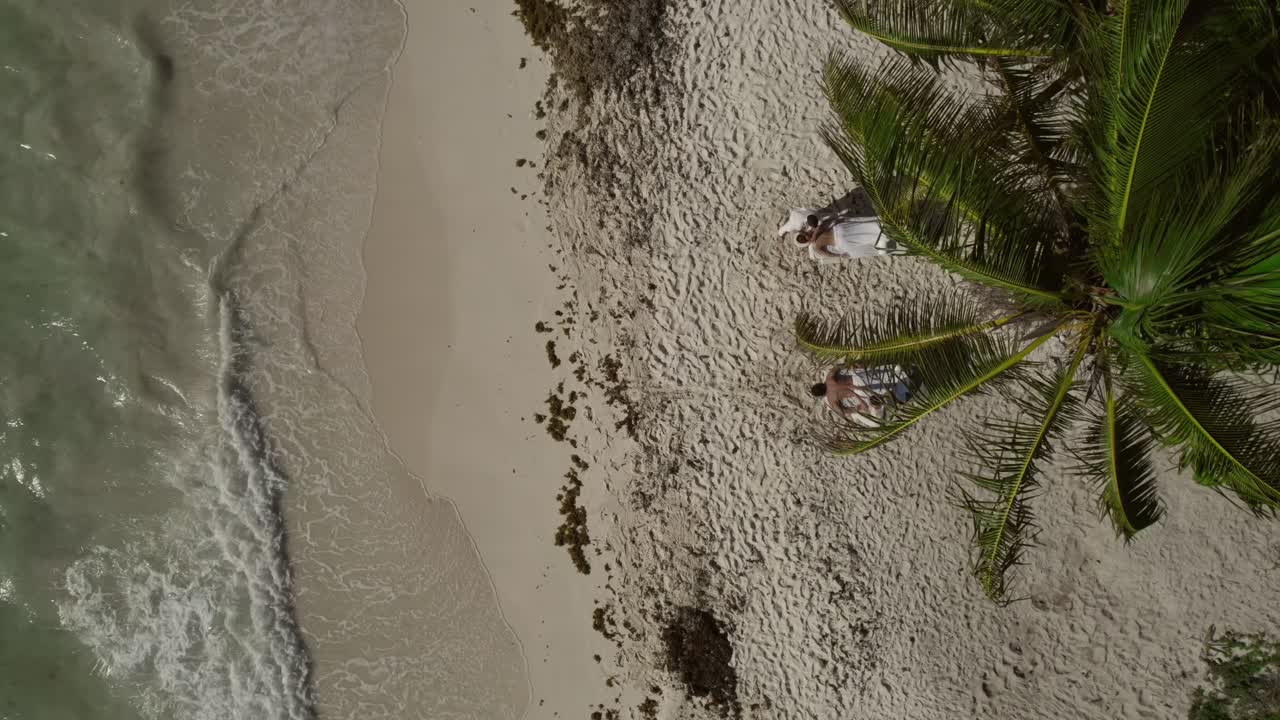 disfruta de la relajación en la playa en riviera maya, méxico, mientras las imágenes de drones capturan a dos personas disfrutando de masajes bajo un cocotero balanceado, con olas relajantes golpeando suavemente la orilla.