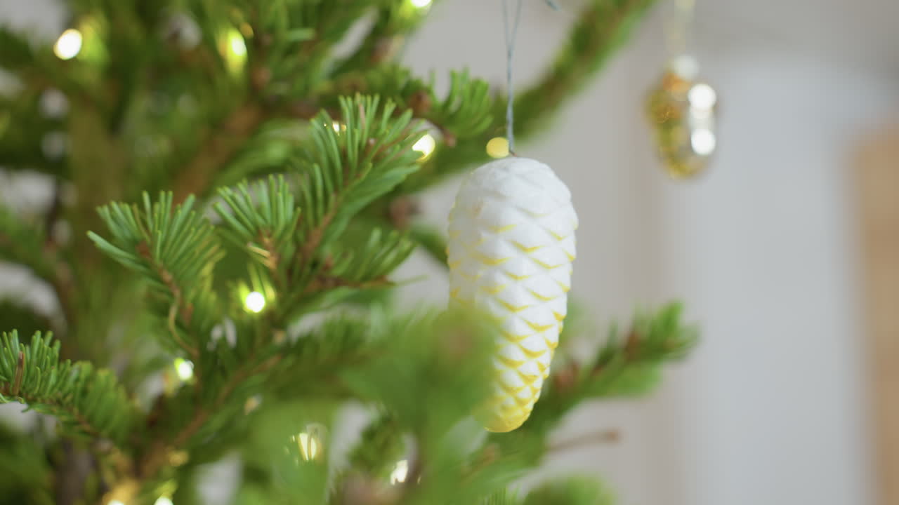 Close view of Christmas tree decorated with vibrant green pine branches and glowing lights, featuring white ornament hanging in center, soft festive indoor atmosphere evoking warmth