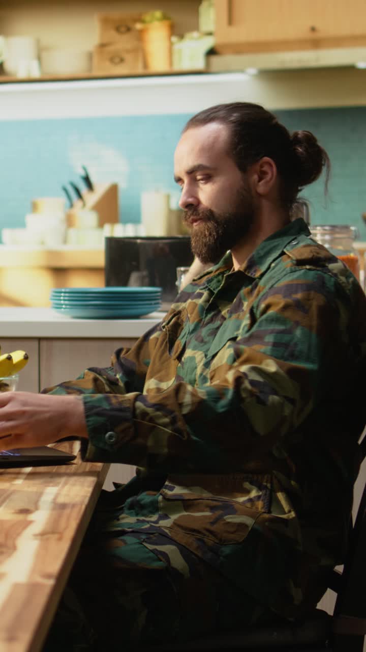 Video Verticale Militare in uniforme fa colazione a casa, servendo caffè e prodotti da forno.