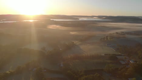 disparo aéreo avanzando sobre tierras de cultivo en el sur de australia con niebla en el paisaje y el amanecer en el horizonte