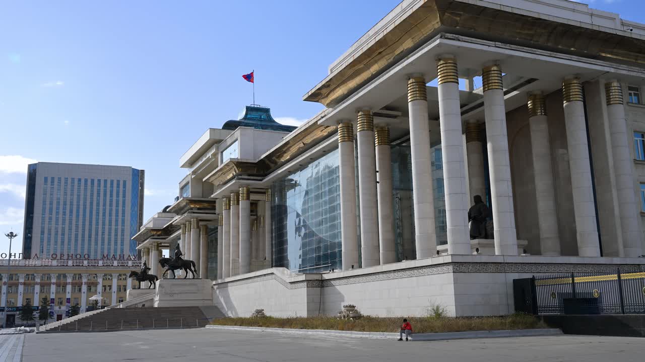 Side view of the Government Palace in Sukhbaatar Square, Ulaanbaatar, Mongolia, with the prominent Mongolian flag and the Genghis Khan statue positioned at its front center.