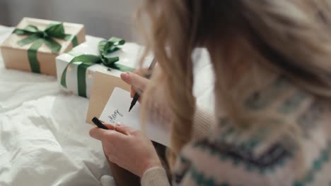 Top-view-of-caucasian-woman-sitting-on-bed-and-writing-Christmas-card