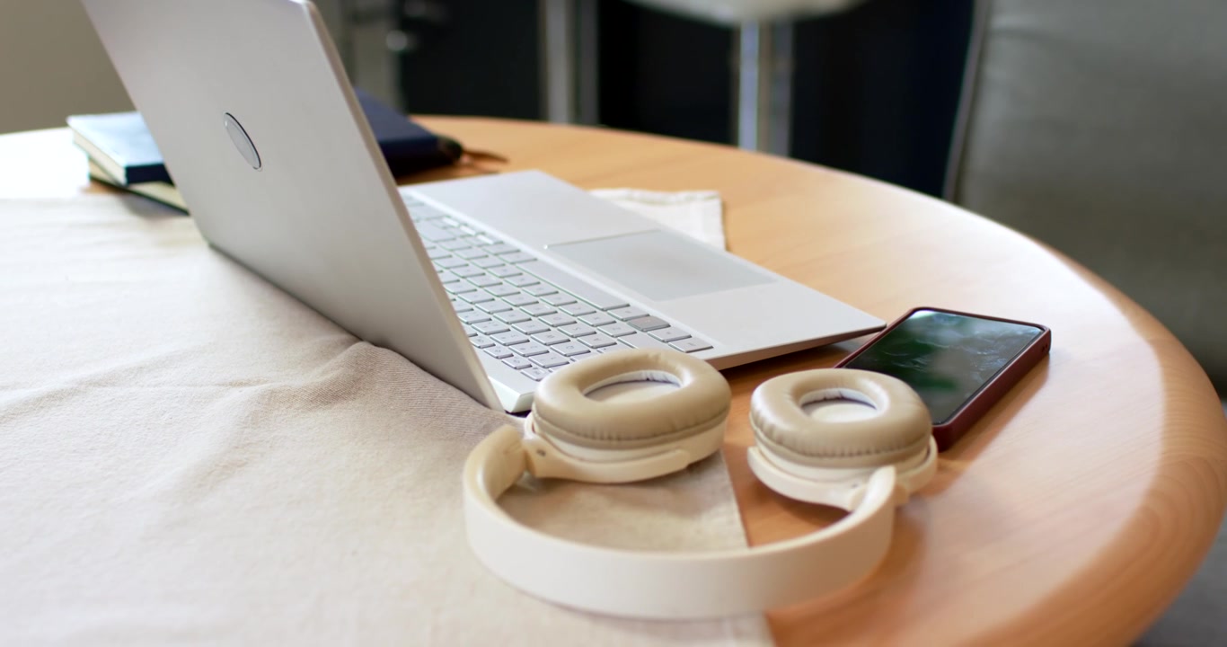 Camera is pulling in, focusing headset; laptop, red-phone blurring on table to highlight headset