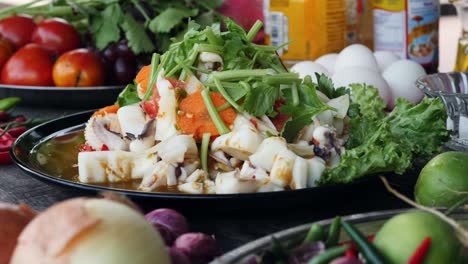 Thai-squid-and-vegetable-dish-on-table-surrounded-by-ingredients,-rotating-shot