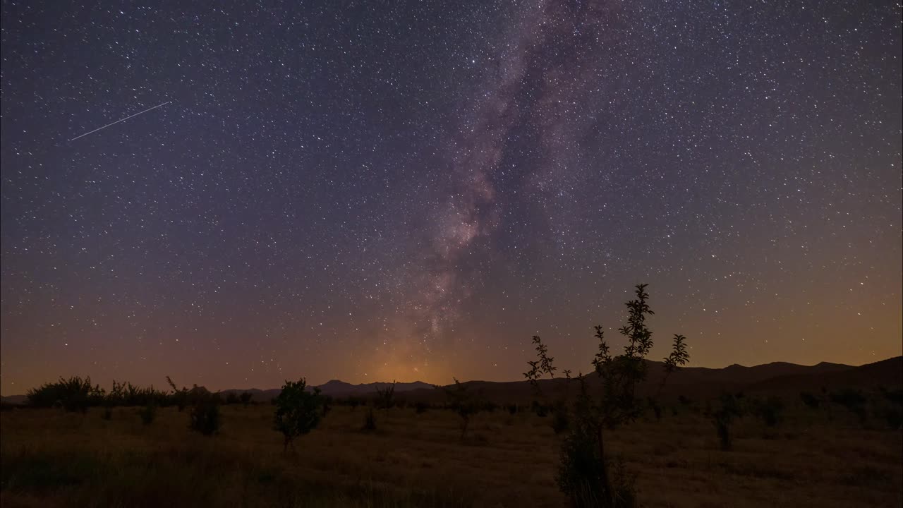 Time-lapse dal cielo notturno stellato al mattino in un giardino pianeggiante con alberi di noci, mele, bacche e pistacchi, e la Via Lattea che brilla e si sposta fino a tramontare all'orizzonte. Agriturismo.