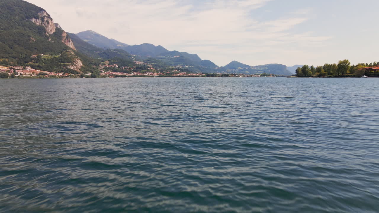 vuelo cinematográfico sobre el agua azul del lago como en italia con montañas y cielo nublado en el fondo - toma aérea de drones