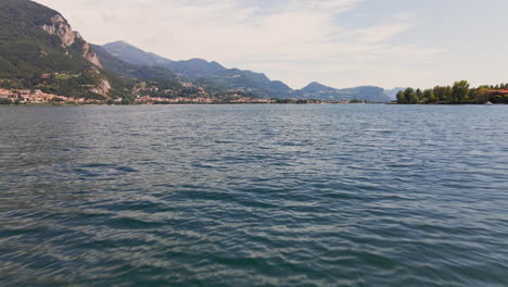 cinematic flight over the blue water of lake como in italy with mountains and cloudy sky in background - aerial drone shot