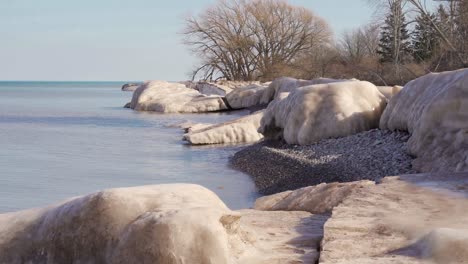 a winter pebble beach with small waves flowing and large melting ice chunks in 4k