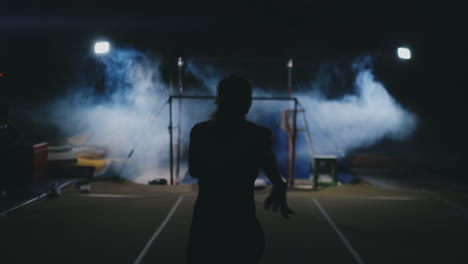 Competitions-in-gymnastics.-A-woman-walks-to-the-crossbar-and-performs-dips-flip-flops-in-slow-motion-on-a-dark-background-in-backlight.-Slow-motion.