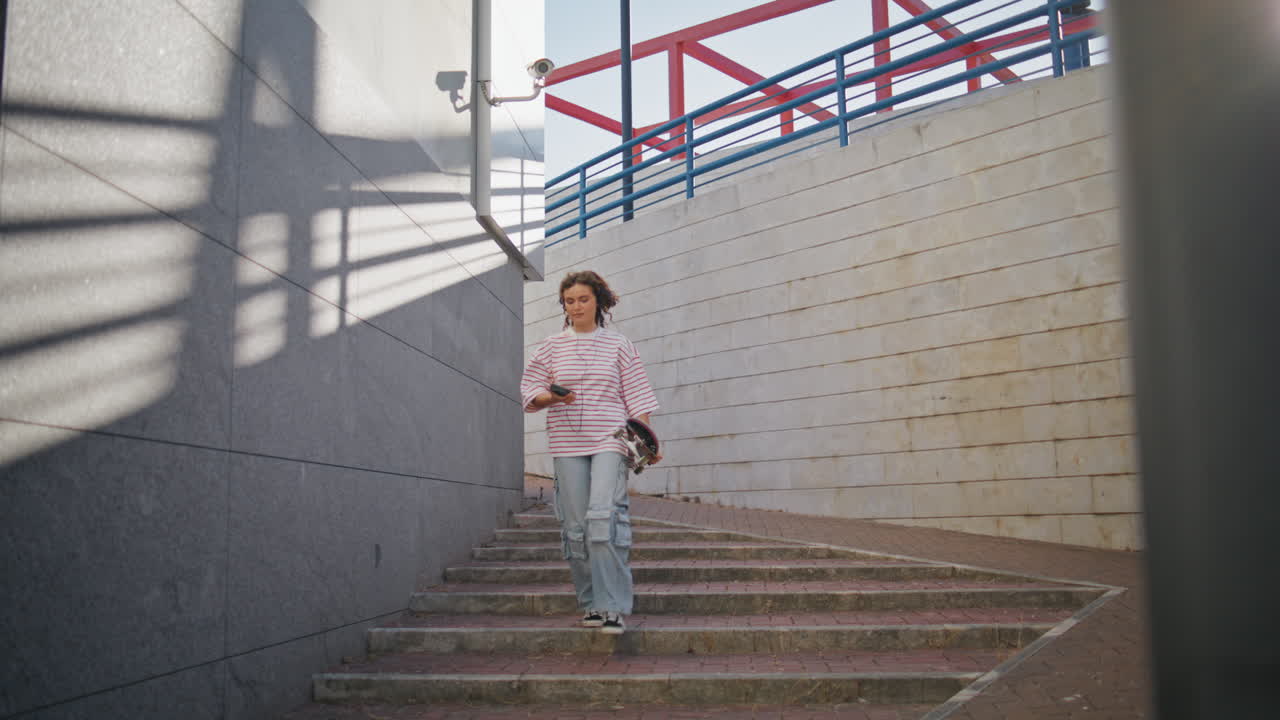 niña patinadora caminando por las escaleras de la ciudad sosteniendo una tabla larga. mujer escuchando música