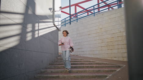 girl skater walking stairs down city holding longboard. woman listening music