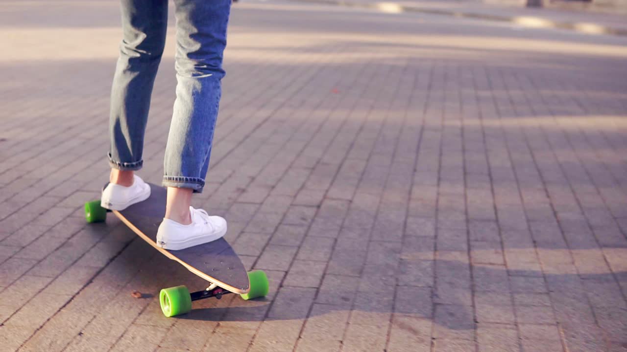 Close Up view of woman's legs in blue jeans and white sneakers starting to skateboard on the longboard in the cobblestone road in